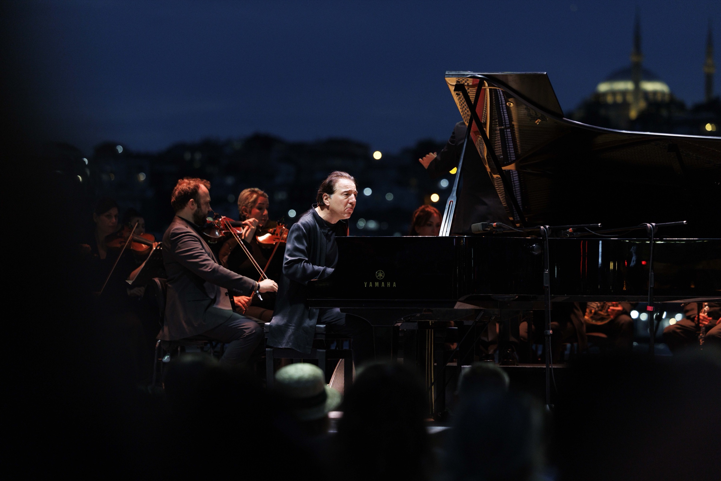Gece açık hava konserinde piyano ve orkestra, arka planda İstanbul silüeti